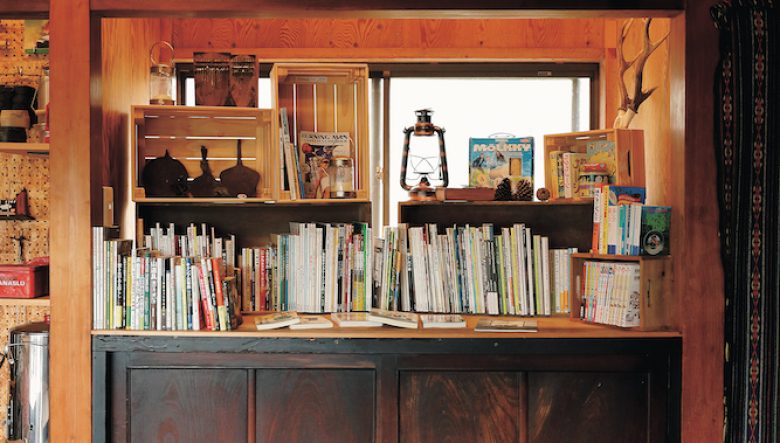 野遊びにまつわる書籍が並ぶ本棚。「個人的に勉強したい内容の本や、お客さんに読んでほしい本を置いています」。本棚の下には天然木で作られた大きな看板を設置。