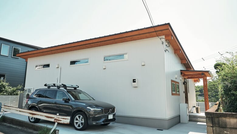 ホワイトのガリバリウム外壁と、ウッドのコントラストが印象的な平屋の裏手を駐車場に。片流れの屋根のため駐車場側は庭側よりも高さがある。積載量重視の愛車はボルボXC90。