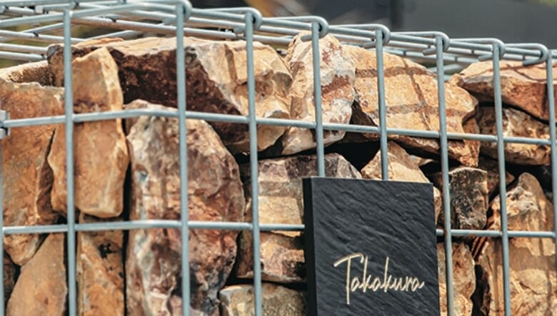 表札を取り付けたガビオンの石は、家の色と相性のいいブラウンをセレクト。多めに石を用意してもらい、フェンス下やアプローチなど、庭全体に配置している。